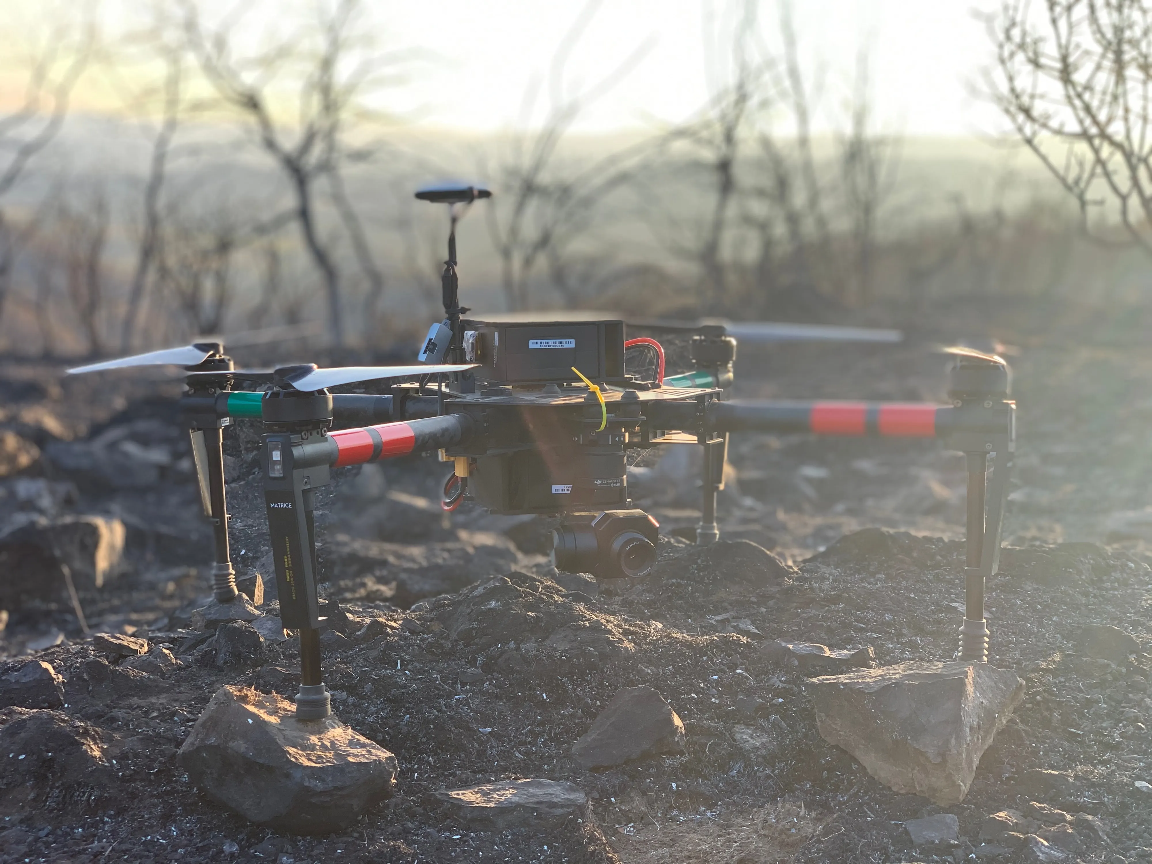 The Matrice 300 sitting on burned ground with smoke drifting behind it.