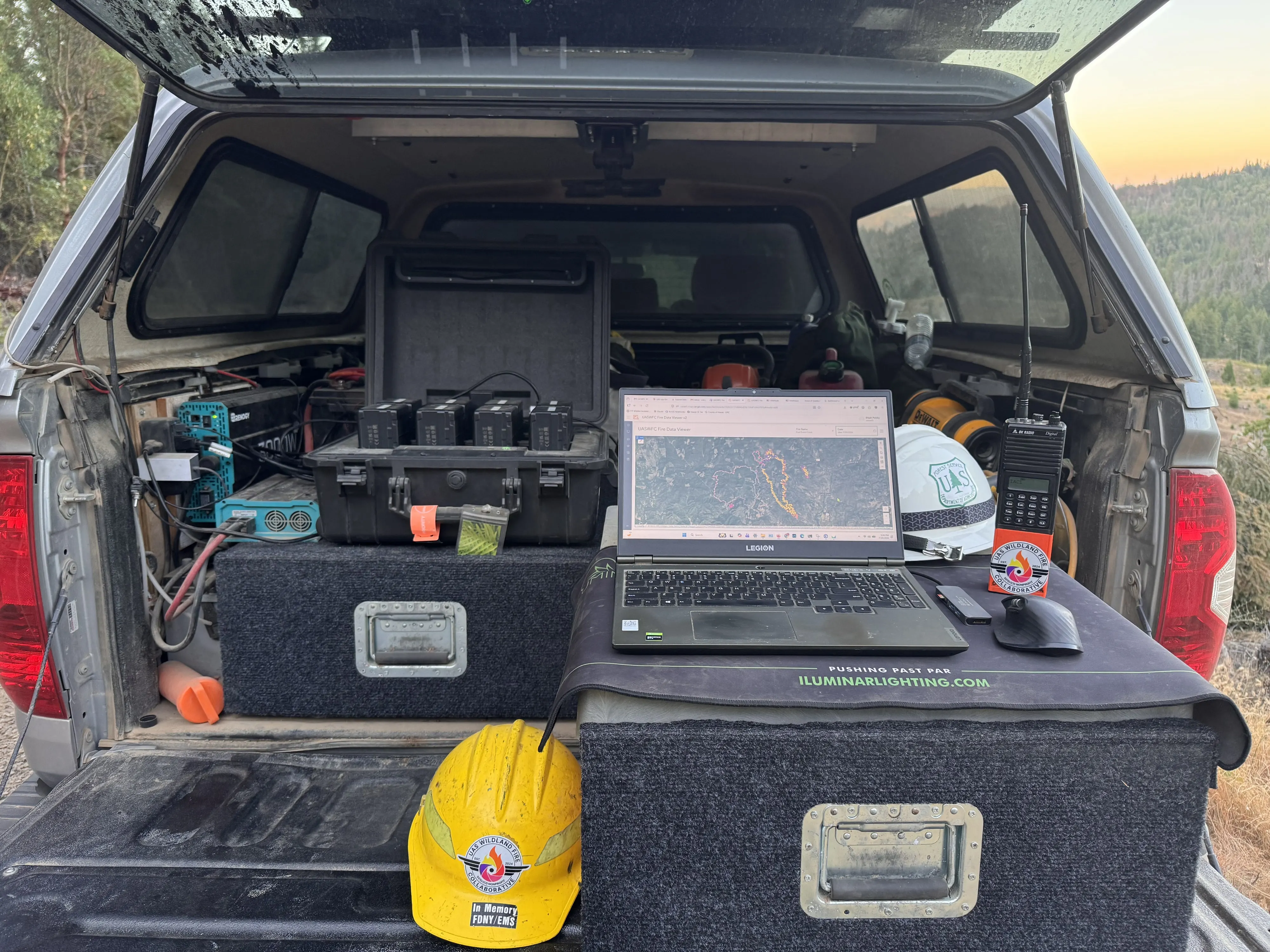 Processing workstation in the back of the truck: laptop, hard cases, helmet, and radios, with the valley behind.