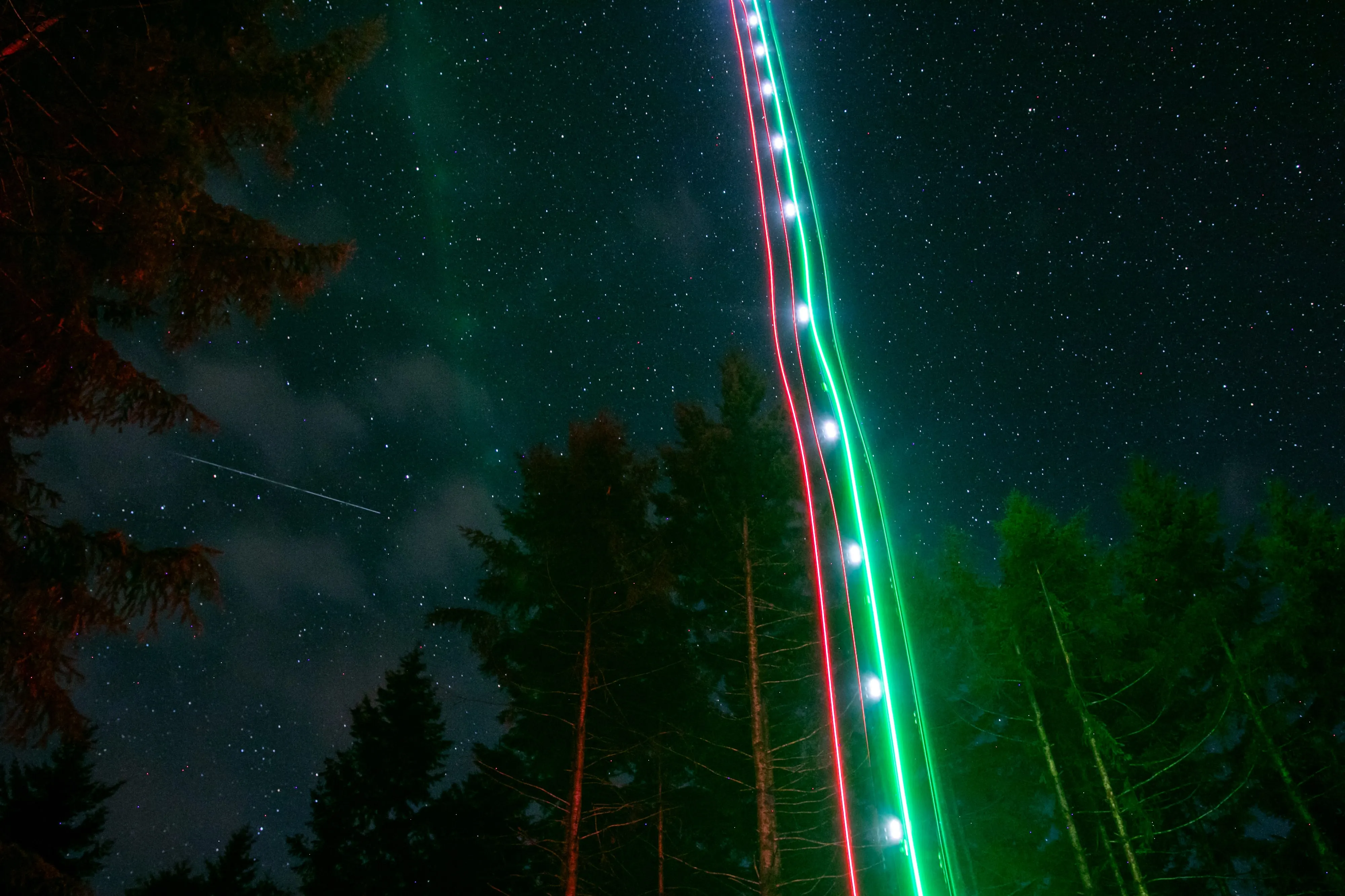 Long exposure at night: the aircraft strobe traces a bright line up through the trees into a starry sky.
