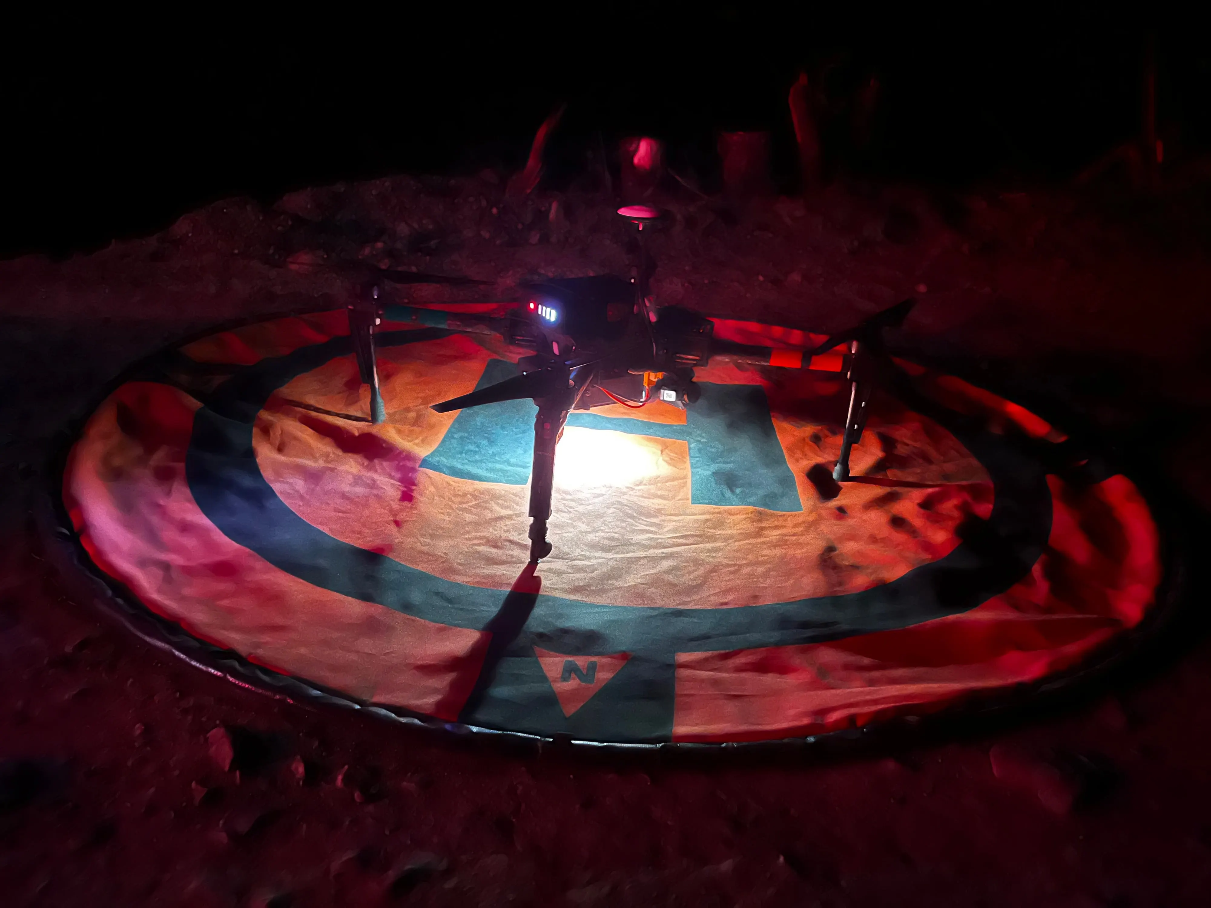 The aircraft on its landing pad at night lit in red.